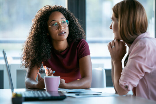 Two women talking, by the table, on the table there is a laptop and purple coffee mug