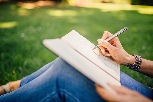 women siting on the grass with the notebook and writing in it